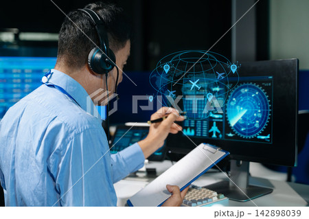 Air traffic control operators wearing headsets monitor live flight radar and navigate airspace data on screens in control center. Air traffic control operators wearing headsets monitor live flight radar and navigate airspace data on screens in control center. 142898039