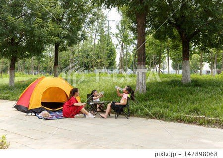 Young family enjoying summer camping in city park with orange tent under green trees 142898068