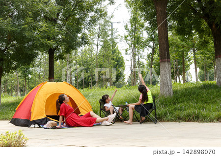 Young family enjoying summer camping in city park with orange tent under green trees 142898070