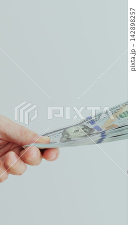 Vertical video. A man hand passes a wad of money to a woman hand. Hundred dollar banknotes. Paying for something. Close-up. Vertical video. A man hand passes a wad of money to a woman hand. Hundred dollar banknotes. Paying for something. Close-up. 142898257
