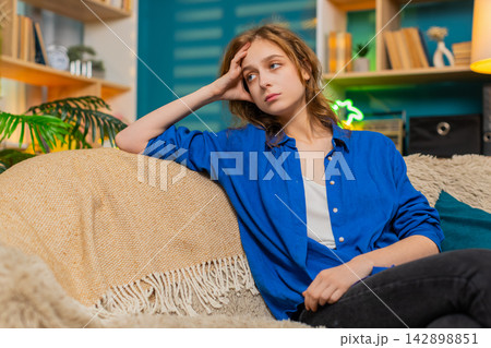 Young woman on home sofa looks tired and emotionally drained with sad stress in cozy home interior 142898851