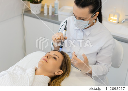 Trichologist doing woman hair regeneration procedure, dermapen microneedling, vitamin injections 142898967