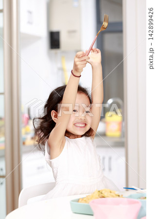 Cute little girl eating food at the dining table, healthy nutrition and child development in daily domestic life. 142899426