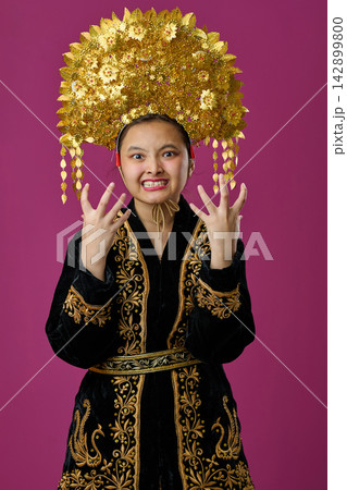 Young Indonesian Asian Girl Wearing Ornate Gold Traditional Headdress and Embroidered Costume Showing Angry Expression Young Indonesian Asian Girl Wearing Ornate Gold Traditional Headdress and Embroidered Costume Showing Angry Expression 142899800