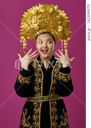 Young Indonesian Asian Girl Wearing Traditional Gold Headdress and Embroidered Robe Celebrating Cultural Costume and Joy Young Indonesian Asian Girl Wearing Traditional Gold Headdress and Embroidered Robe Celebrating Cultural Costume and Joy 142899870