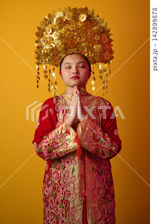 Young Indonesian Asian Girl in Red Embroidered Traditional Costume With Gold Headdress Praying With Eyes Closed Young Indonesian Asian Girl in Red Embroidered Traditional Costume With Gold Headdress Praying With Eyes Closed 142899878