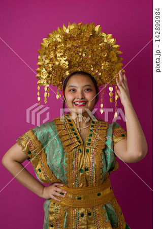 Smiling Indonesian Asian Woman Wearing Ornate Gold Headdress And Traditional Embroidered Costume For Cultural Festival Smiling Indonesian Asian Woman Wearing Ornate Gold Headdress And Traditional Embroidered Costume For Cultural Festival 142899984