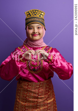 Young Muslim Indonesian Asian Woman in Traditional Pink Costume and Hijab Making a Heart Gesture While Smiling Young Muslim Indonesian Asian Woman in Traditional Pink Costume and Hijab Making a Heart Gesture While Smiling 142899991