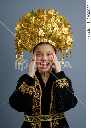 Young Indonesian Asian Woman Wearing Ornate Gold Traditional Headdress and Embroidered Costume, Expressive Portrait Young Indonesian Asian Woman Wearing Ornate Gold Traditional Headdress and Embroidered Costume, Expressive Portrait 142900035