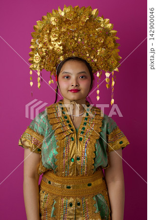 Young Indonesian Asian Woman Portrait in Traditional Golden Headdress and Embroidered Costume Against Pink Background 142900046