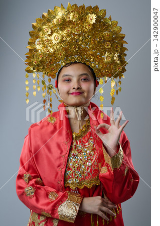 Young Indonesian Asian Girl in Ornate Gold Headdress and Red Traditional Costume Smiling in Portrait Young Indonesian Asian Girl in Ornate Gold Headdress and Red Traditional Costume Smiling in Portrait 142900047