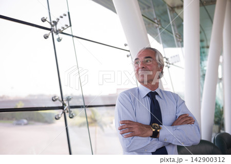 Senior business executive standing confidently in modern glass office with arms crossed Senior business executive standing confidently in modern glass office with arms crossed 142900312