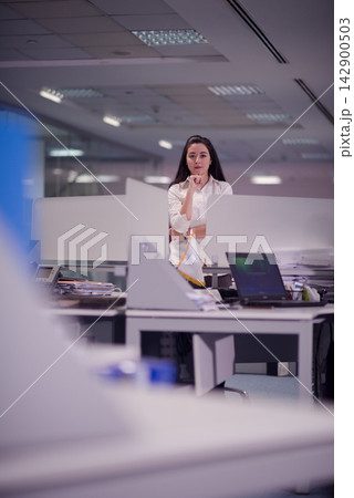 Professional woman standing in a modern open-plan office during a thoughtful business moment 142900503