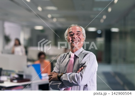 Confident senior businessman smiling in modern open plan office with colleagues and leadership presence 142900504