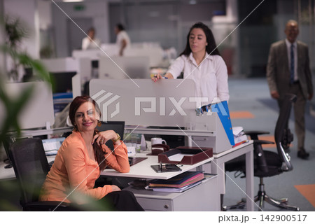 Smiling businesswoman at her desk in a modern open-plan office with colleagues in background 142900517
