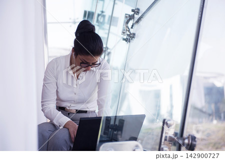 Businesswoman working on laptop in modern glass office with earphones during a meeting Businesswoman working on laptop in modern glass office with earphones during a meeting 142900727