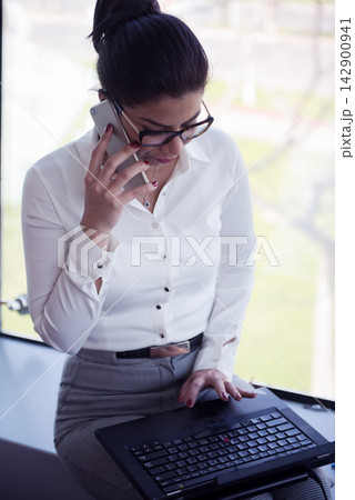 Professional woman on phone working on laptop in a bright modern office workspace Professional woman on phone working on laptop in a bright modern office workspace 142900941