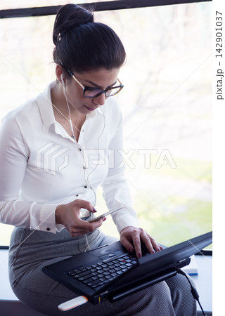Professional businesswoman multitasking with laptop and smartphone while working in a modern open-plan office Professional businesswoman multitasking with laptop and smartphone while working in a modern open-plan office 142901037