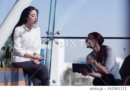 Two business professionals discussing strategy in a modern glass office using a tablet during meeting Two business professionals discussing strategy in a modern glass office using a tablet during meeting 142901115