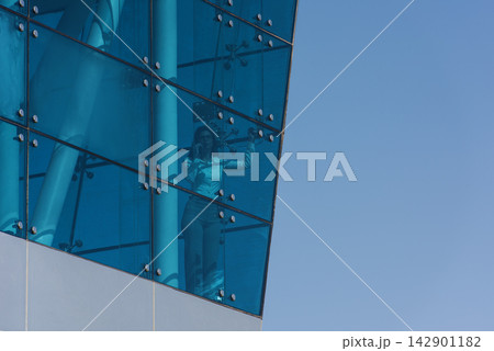 Businesswoman on phone behind blue glass in modern corporate office atrium with reflective facade 142901182