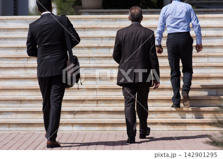 Business professionals walking up outdoor steps toward a modern office building for a corporate meeting 142901295