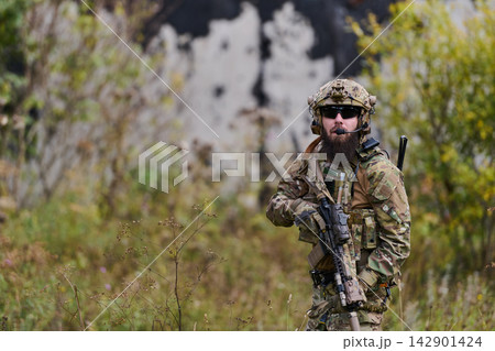 Bearded Soldier in Camo Tactical Gear With Rifle Patrolling Overgrown Field During Military Exercise Bearded Soldier in Camo Tactical Gear With Rifle Patrolling Overgrown Field During Military Exercise 142901424