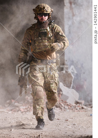 Armed Soldier In Tactical Gear Running Through Dusty Urban Combat Ruins With Rifle And Helmet Armed Soldier In Tactical Gear Running Through Dusty Urban Combat Ruins With Rifle And Helmet 142901441