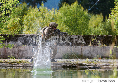 Camouflaged Soldier Firing Rifle During Tactical Training Beside Forest Pond With Water Splash 142901559