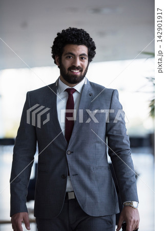 Confident young businessman in gray suit smiling while walking through modern office lobby 142901917