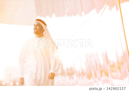 Middle Eastern businessman in traditional kandura walking confidently through modern corporate open space at meeting 142902157