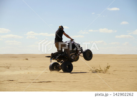 Young quad bike rider doing wheelie in desert 142902262