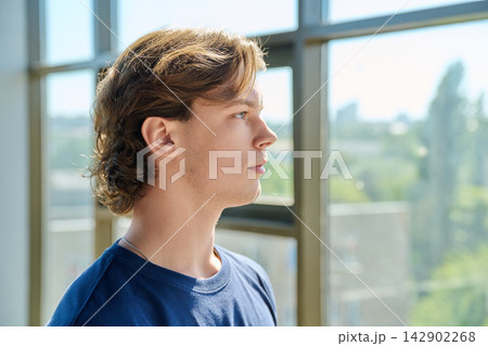 Side view profile portrait of handsome young man looking up near large window 142902268