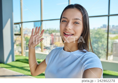 Young smiling female student making selfie video call and waving hand 142902278
