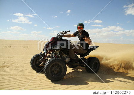 Young quad bike rider doing wheelie in desert 142902279