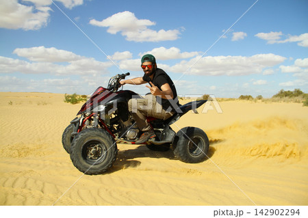 Young quad bike rider doing wheelie in desert 142902294