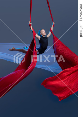 Teen aerialist opening arms between flowing silks 142902508