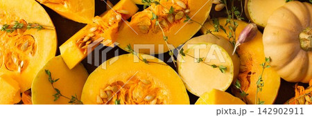 The scene shows various pieces of cut squash placed on a wooden table. Fresh thyme sprigs are scattered among the squash. Natural light fills the area, emphasizing the colors, banner The scene shows various pieces of cut squash placed on a wooden table. Fresh thyme sprigs are scattered among the squash. Natural light fills the area, emphasizing the colors, banner 142902911
