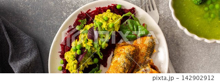 Baked small sea fish is served alongside boiled beets, hummus, green peas, and herbs. This dish is suitable for breakfast and offers a healthy option, banner 142902912