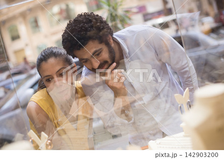Couple choosing a wedding ring while window shopping at a jewelry store, sharing a tender moment Couple choosing a wedding ring while window shopping at a jewelry store, sharing a tender moment 142903200