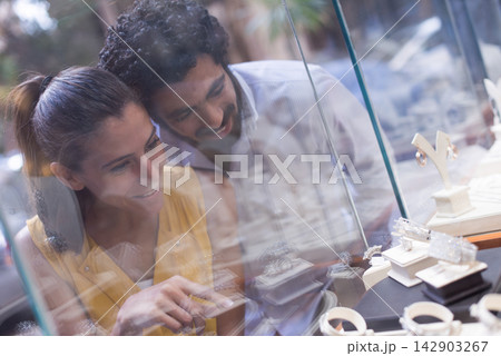Middle Eastern couple shopping for a wedding ring together at a jewelry store display with smiles Middle Eastern couple shopping for a wedding ring together at a jewelry store display with smiles 142903267