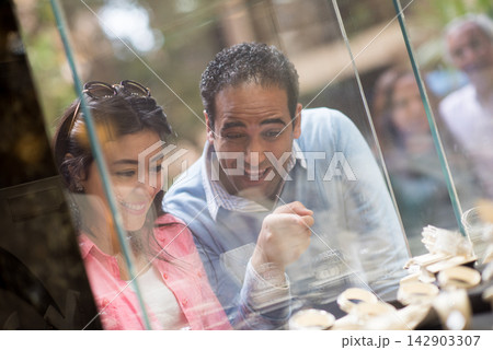 Happy couple choosing wedding rings together at a jewelry shop with smiling friends and family nearby 142903307