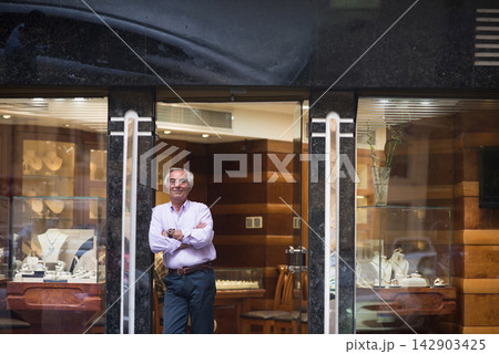 Jewelry store owner standing in shop doorway with displays of engagement and wedding rings 142903425