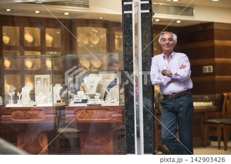 Middle Eastern jewelry shop owner standing by display as couple shops for wedding rings with family Middle Eastern jewelry shop owner standing by display as couple shops for wedding rings with family 142903426