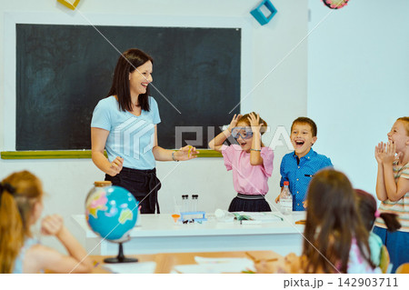 Teacher leading a joyful classroom science experiment with excited elementary students gathered around a desk Teacher leading a joyful classroom science experiment with excited elementary students gathered around a desk 142903711