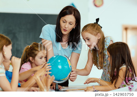 Elementary teacher showing globe to engaged students in classroom geography lesson Elementary teacher showing globe to engaged students in classroom geography lesson 142903750