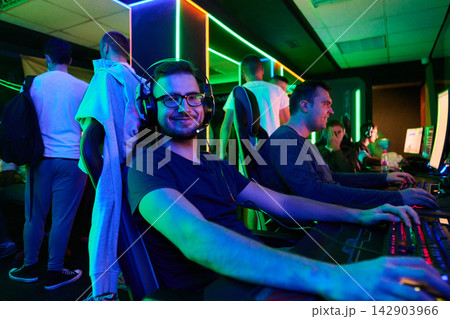 Young Gamers Smiling in Neon Gaming Lounge Wearing Headsets During Team Computer Tournament Session Young Gamers Smiling in Neon Gaming Lounge Wearing Headsets During Team Computer Tournament Session 142903966