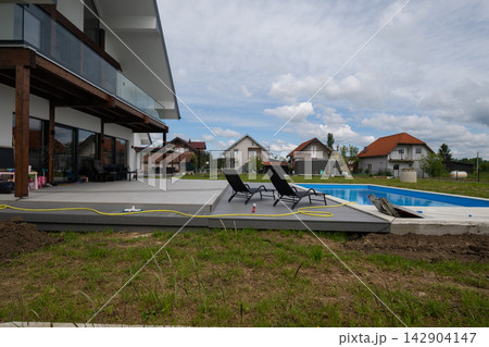 Modern suburban house with patio, swimming pool and lounge chairs on a cloudy summer day 142904147