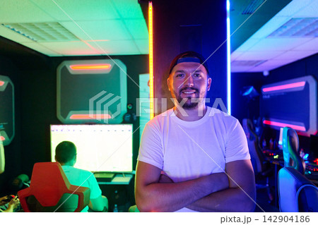 Confident Gamer Standing in Neon-Lit Esports Gaming Room With Computers and Team Players Confident Gamer Standing in Neon-Lit Esports Gaming Room With Computers and Team Players 142904186