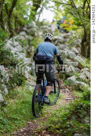 Mountain biker riding a rocky forest trail uphill on a blue mountain bike 142904281