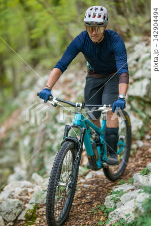 Man mountain biking on rocky forest trail wearing helmet and protective gear Man mountain biking on rocky forest trail wearing helmet and protective gear 142904494
